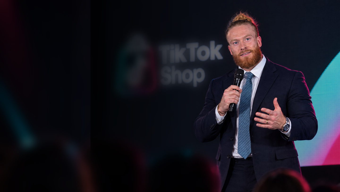 Dr. Stevan Stabelin no palco, de microfone, diante do telão do TikTok Shop